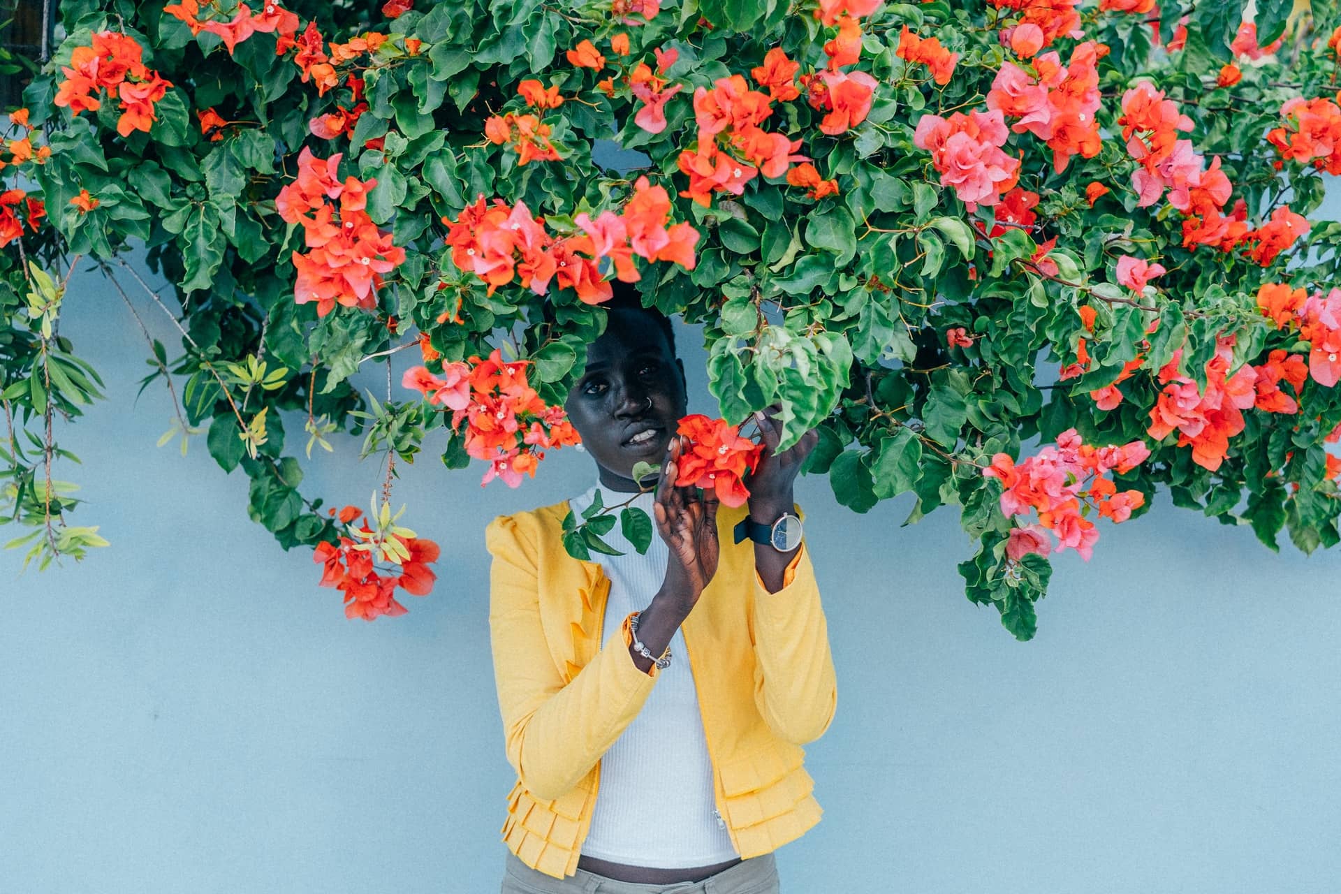 Black woman in yellow coat poses under a blossoming bush.