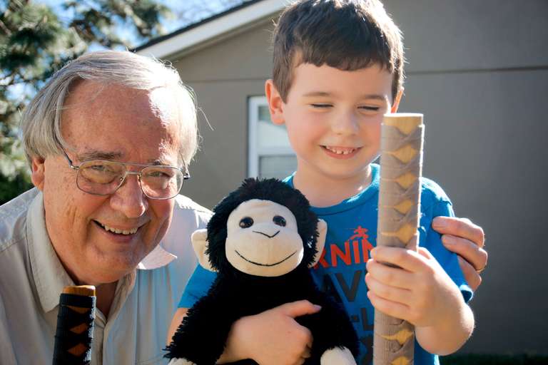 Dan Hopkins with grandson, holding wooden samurai swords.