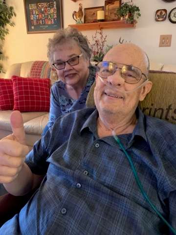 Dan reclining and holding a thumbs up next to his sister.